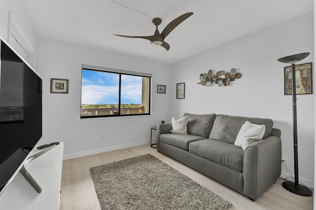 living area with light wood-type flooring, a ceiling fan, and baseboards