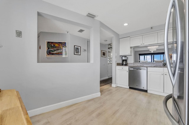 kitchen with light wood finished floors, baseboards, white cabinets, visible vents, and stainless steel appliances