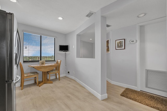 dining area with baseboards, a textured ceiling, visible vents, and light wood-style floors