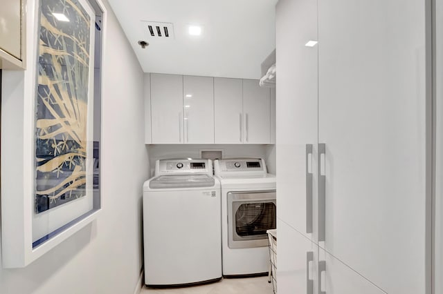 clothes washing area with visible vents, cabinet space, and washing machine and dryer