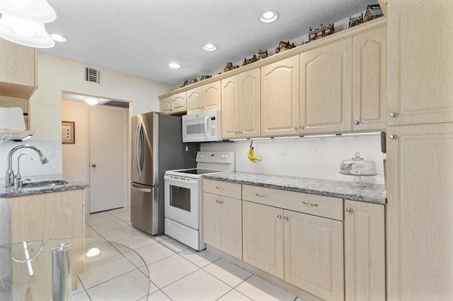 kitchen featuring white appliances, visible vents, light stone counters, light brown cabinets, and a sink