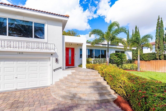 entrance to property with a garage, fence, and stucco siding