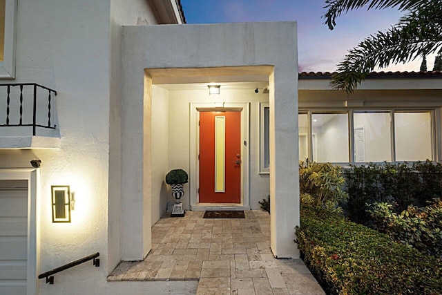 exterior entry at dusk with a tiled roof and stucco siding