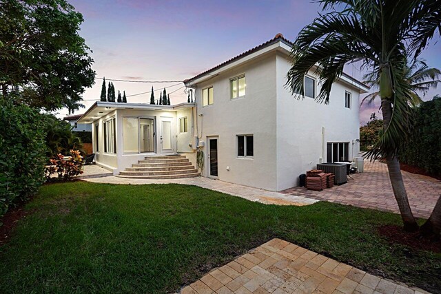 rear view of house with a lawn, a sunroom, cooling unit, a patio area, and stucco siding