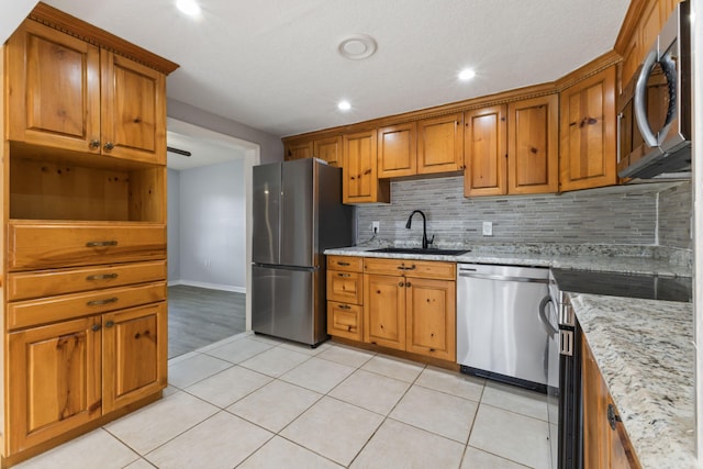 kitchen with light tile patterned floors, light stone countertops, stainless steel appliances, a sink, and brown cabinets