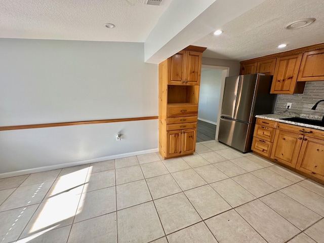 kitchen with light tile patterned floors, tasteful backsplash, freestanding refrigerator, a sink, and baseboards