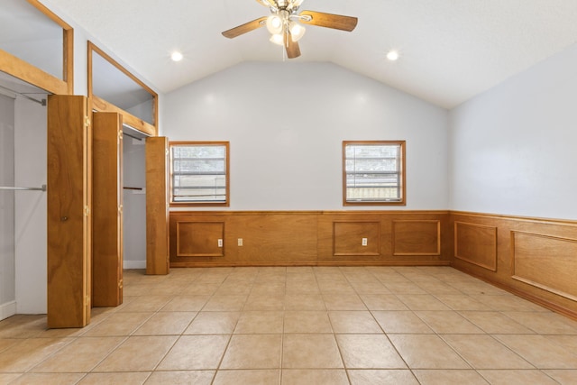 unfurnished room featuring vaulted ceiling, light tile patterned flooring, wainscoting, and a wealth of natural light