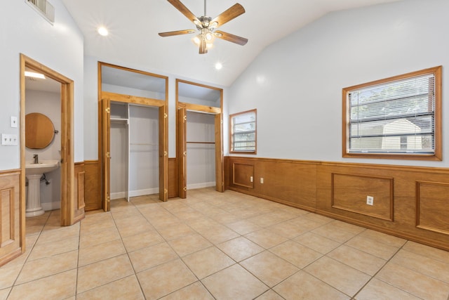 unfurnished bedroom featuring a wainscoted wall, visible vents, vaulted ceiling, and light tile patterned floors