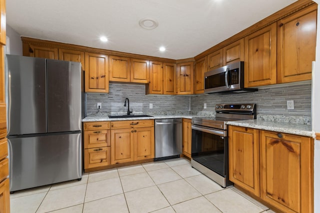 kitchen with appliances with stainless steel finishes, brown cabinets, a sink, and light stone countertops