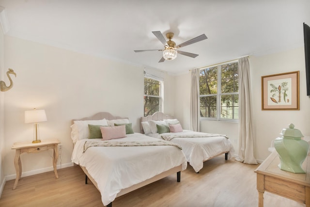 bedroom featuring light wood finished floors, ceiling fan, baseboards, and ornamental molding