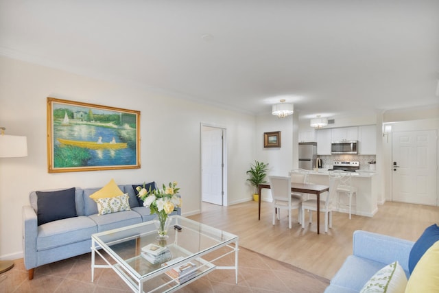 living room featuring light wood-style floors, baseboards, crown molding, and an inviting chandelier