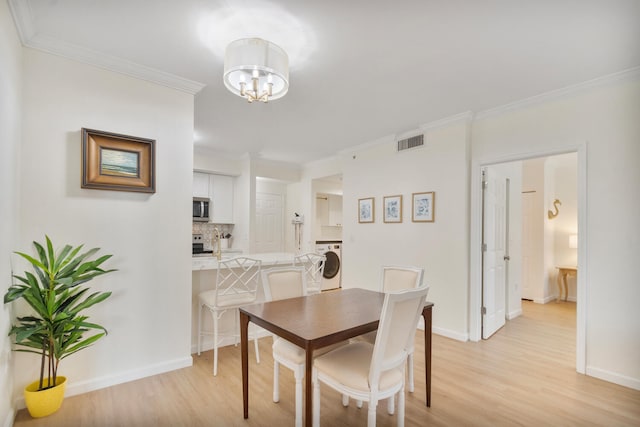 dining area with visible vents, baseboards, ornamental molding, light wood-type flooring, and washer / dryer