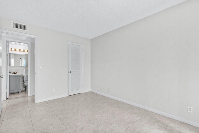 unfurnished bedroom featuring visible vents, a textured ceiling, baseboards, and light tile patterned flooring