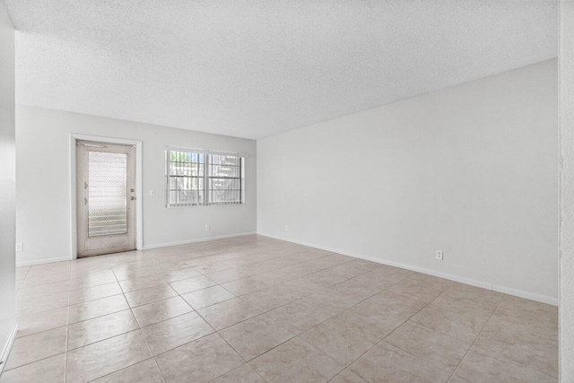 spare room featuring light tile patterned floors, baseboards, and a textured ceiling