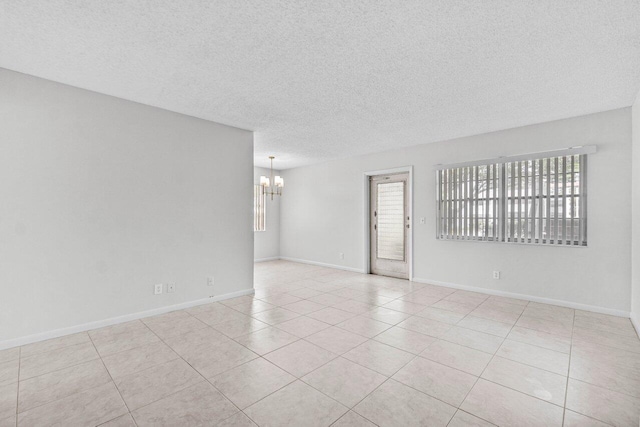 tiled empty room with baseboards, a chandelier, and a textured ceiling