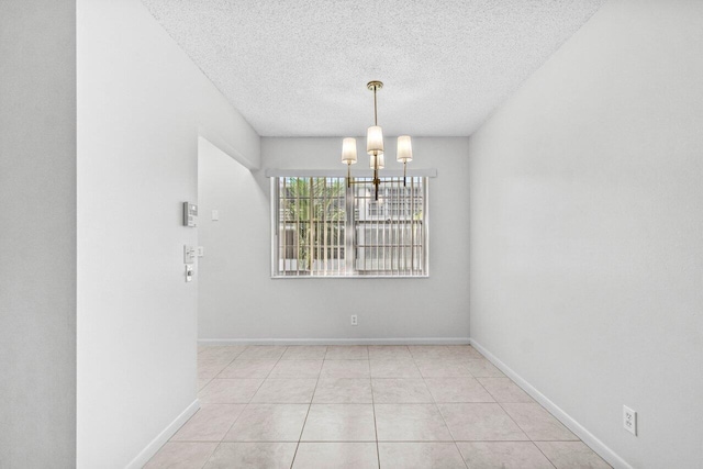 spare room with a chandelier, light tile patterned floors, a textured ceiling, and baseboards