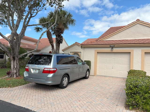 view of front facade with decorative driveway, an attached garage, a tile roof, and stucco siding