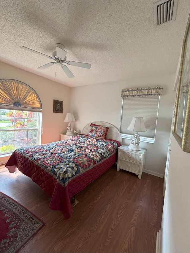 bedroom featuring a textured ceiling, wood finished floors, visible vents, baseboards, and a ceiling fan