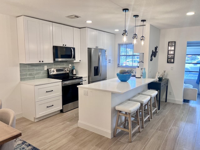 kitchen featuring light wood finished floors, stainless steel appliances, tasteful backsplash, visible vents, and a kitchen breakfast bar