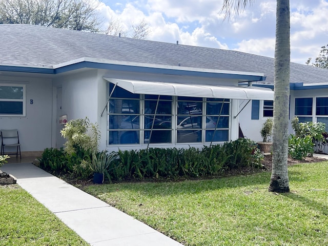 exterior space featuring roof with shingles, a front lawn, and stucco siding