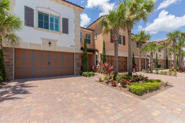 mediterranean / spanish-style house featuring stone siding, decorative driveway, an attached garage, and stucco siding