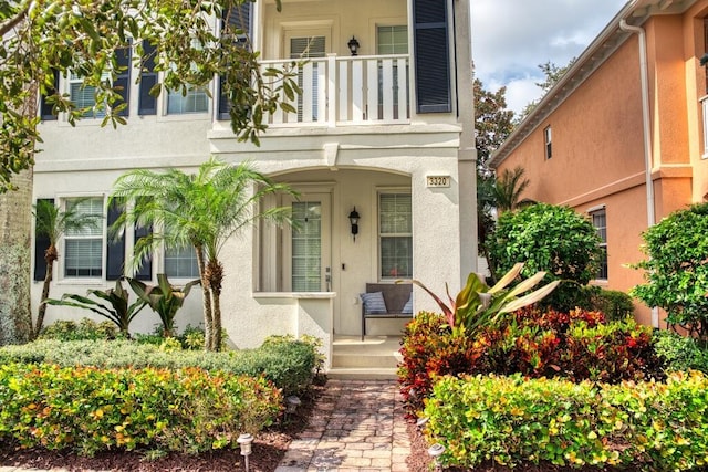 property entrance featuring covered porch, a balcony, and stucco siding