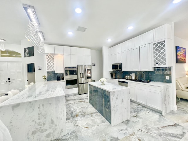 kitchen featuring stainless steel appliances, a sink, marble finish floor, light stone countertops, and tasteful backsplash