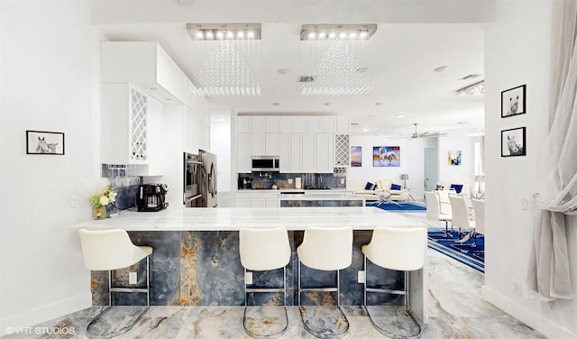 kitchen featuring a peninsula, a ceiling fan, white cabinets, stainless steel microwave, and baseboards