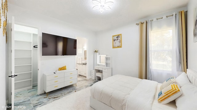 bedroom with a spacious closet, ensuite bathroom, marble finish floor, and a textured ceiling