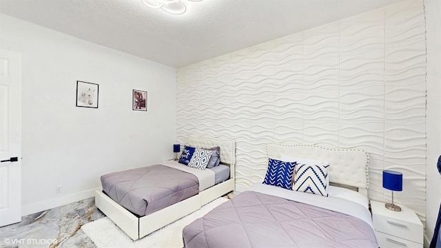 bedroom with an accent wall, marble finish floor, baseboards, and a textured ceiling