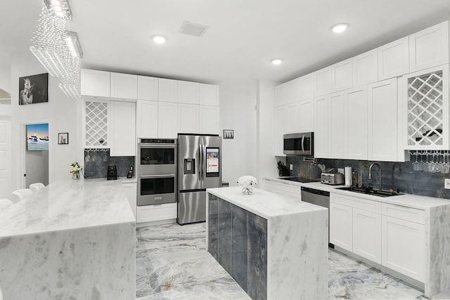 kitchen featuring a peninsula, marble finish floor, a sink, stainless steel appliances, and backsplash