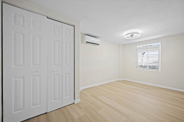 unfurnished bedroom with light wood-style floors, a closet, baseboards, and an AC wall unit