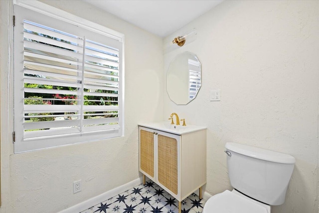 bathroom featuring a textured wall, toilet, vanity, baseboards, and tile patterned floors