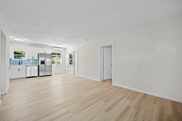 unfurnished living room featuring light wood finished floors, baseboards, and a sink