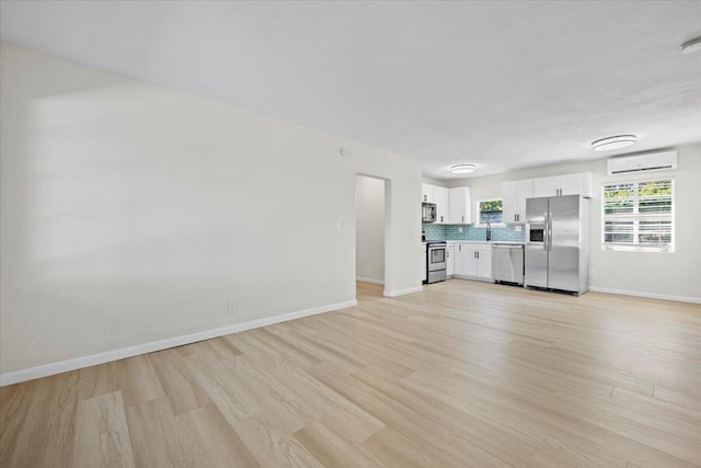 unfurnished living room featuring a wall unit AC, light wood-type flooring, and baseboards