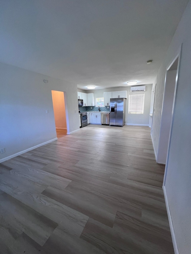 unfurnished living room featuring an AC wall unit, baseboards, a sink, and light wood finished floors