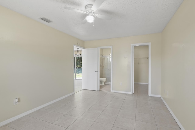 unfurnished bedroom with a textured ceiling, a spacious closet, light tile patterned floors, and baseboards