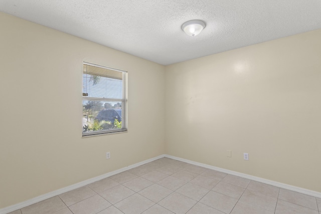 empty room featuring a textured ceiling, baseboards, and light tile patterned floors