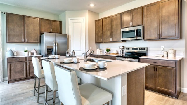 kitchen with a center island with sink, a kitchen breakfast bar, stainless steel appliances, wood finish floors, and a sink