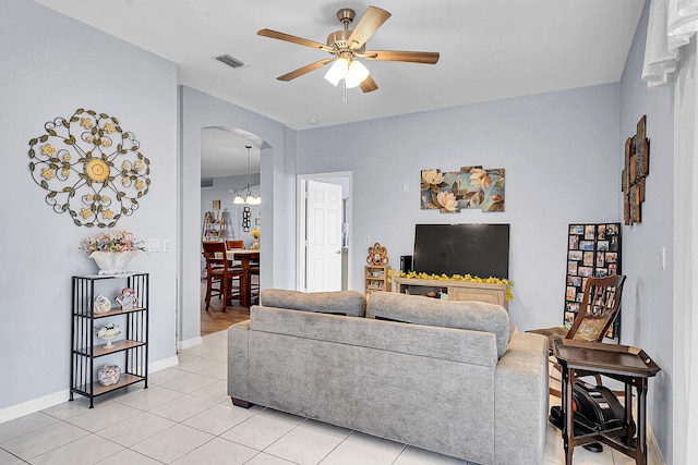 living room featuring arched walkways, visible vents, light tile patterned flooring, baseboards, and ceiling fan with notable chandelier