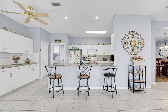 kitchen with arched walkways, white appliances, visible vents, and a kitchen breakfast bar