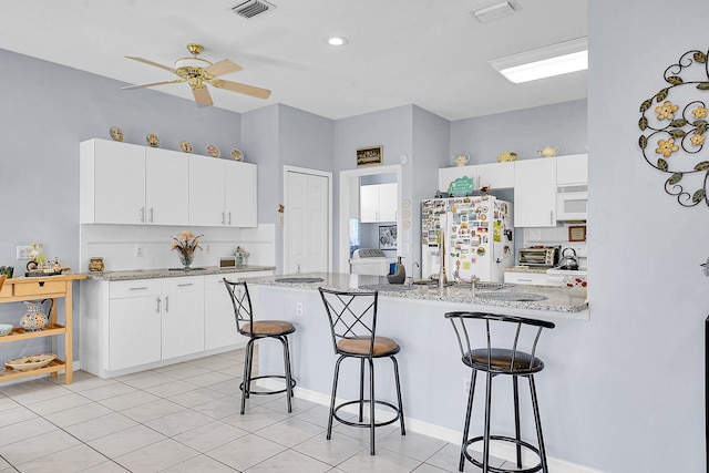 kitchen featuring visible vents, a peninsula, white appliances, and a breakfast bar