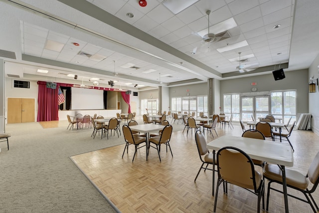 dining space featuring carpet floors, visible vents, ceiling fan, and a drop ceiling