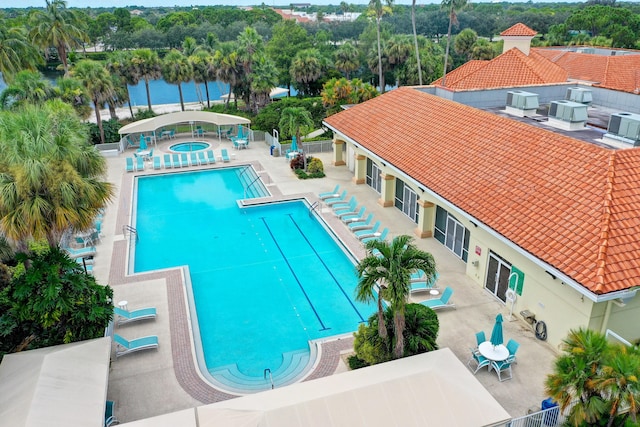 community pool featuring a patio, a water view, fence, and a hot tub