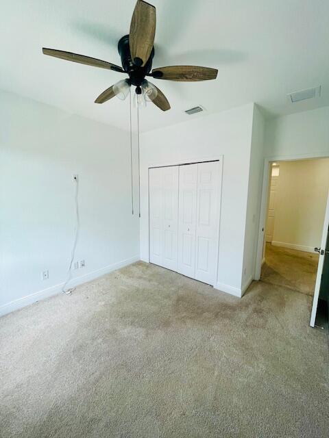 unfurnished bedroom featuring carpet flooring, a ceiling fan, visible vents, baseboards, and a closet