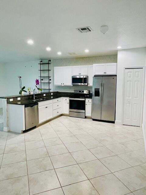 kitchen featuring stainless steel appliances, dark countertops, visible vents, white cabinets, and a peninsula