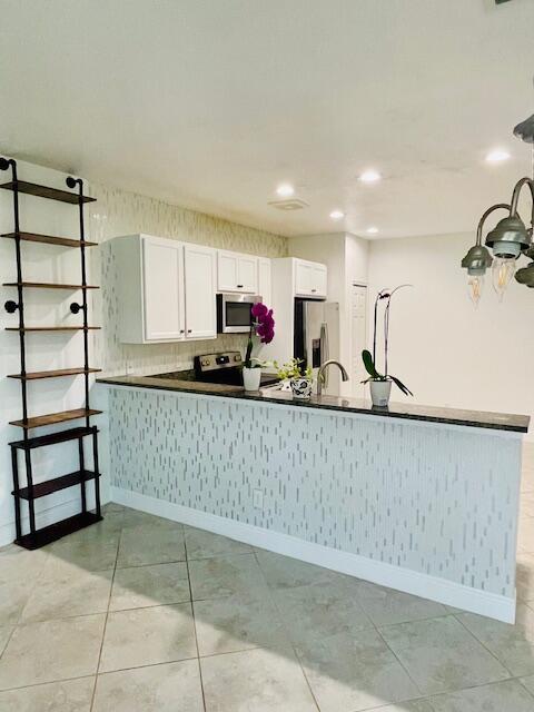 kitchen with appliances with stainless steel finishes, dark countertops, white cabinets, and a peninsula