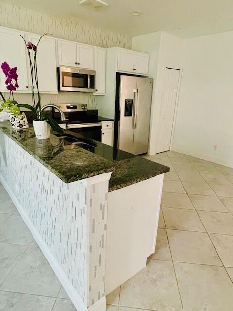 kitchen featuring light tile patterned flooring, stainless steel appliances, white cabinetry, baseboards, and dark stone countertops