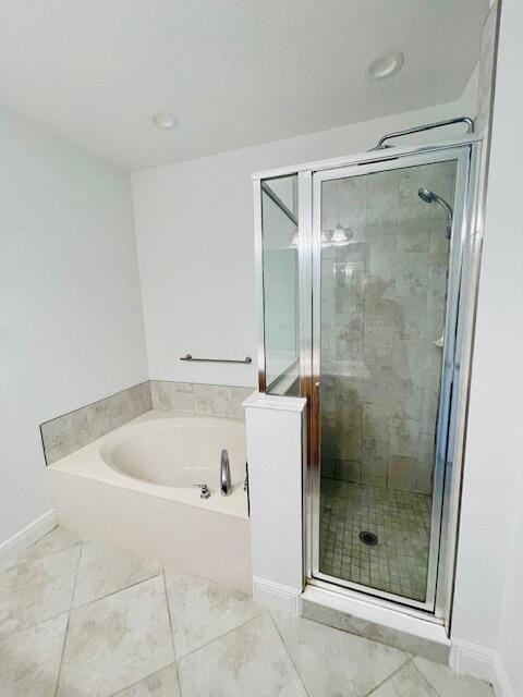 bathroom with a garden tub, a shower stall, and baseboards