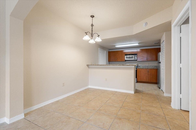 kitchen with light tile patterned floors, stainless steel appliances, brown cabinetry, a textured ceiling, and a peninsula